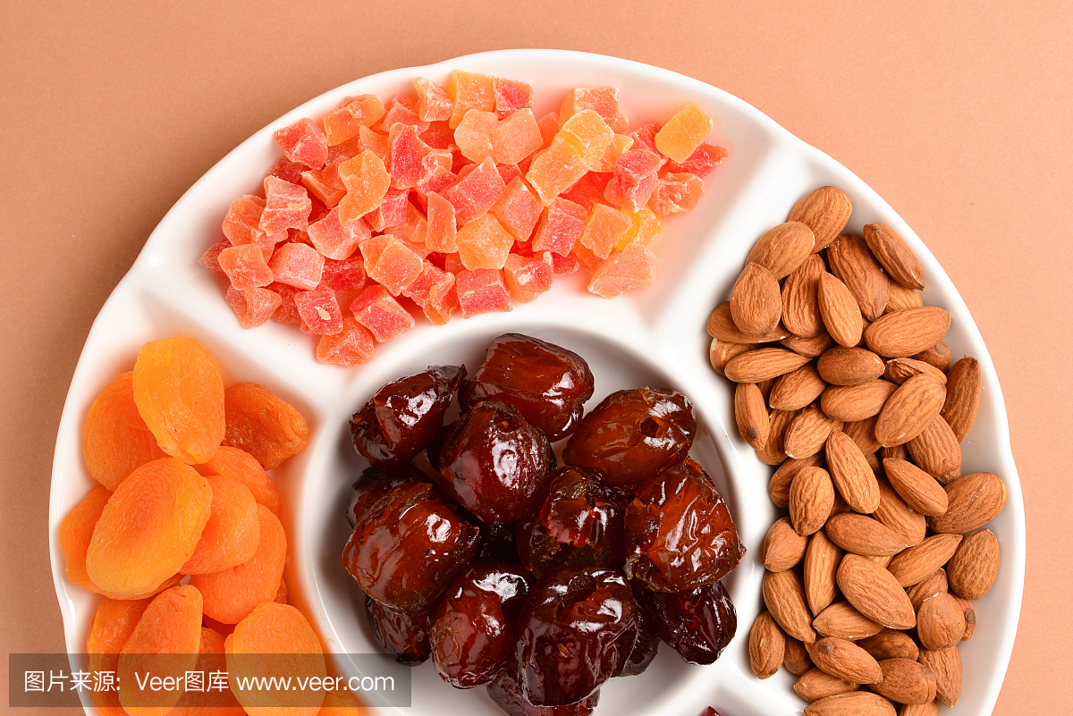 将干果和坚果混合放在一个白色盘子里。杏,杏仁,葡萄干,红枣水果。在棕色的背景上。文字或设计空间。